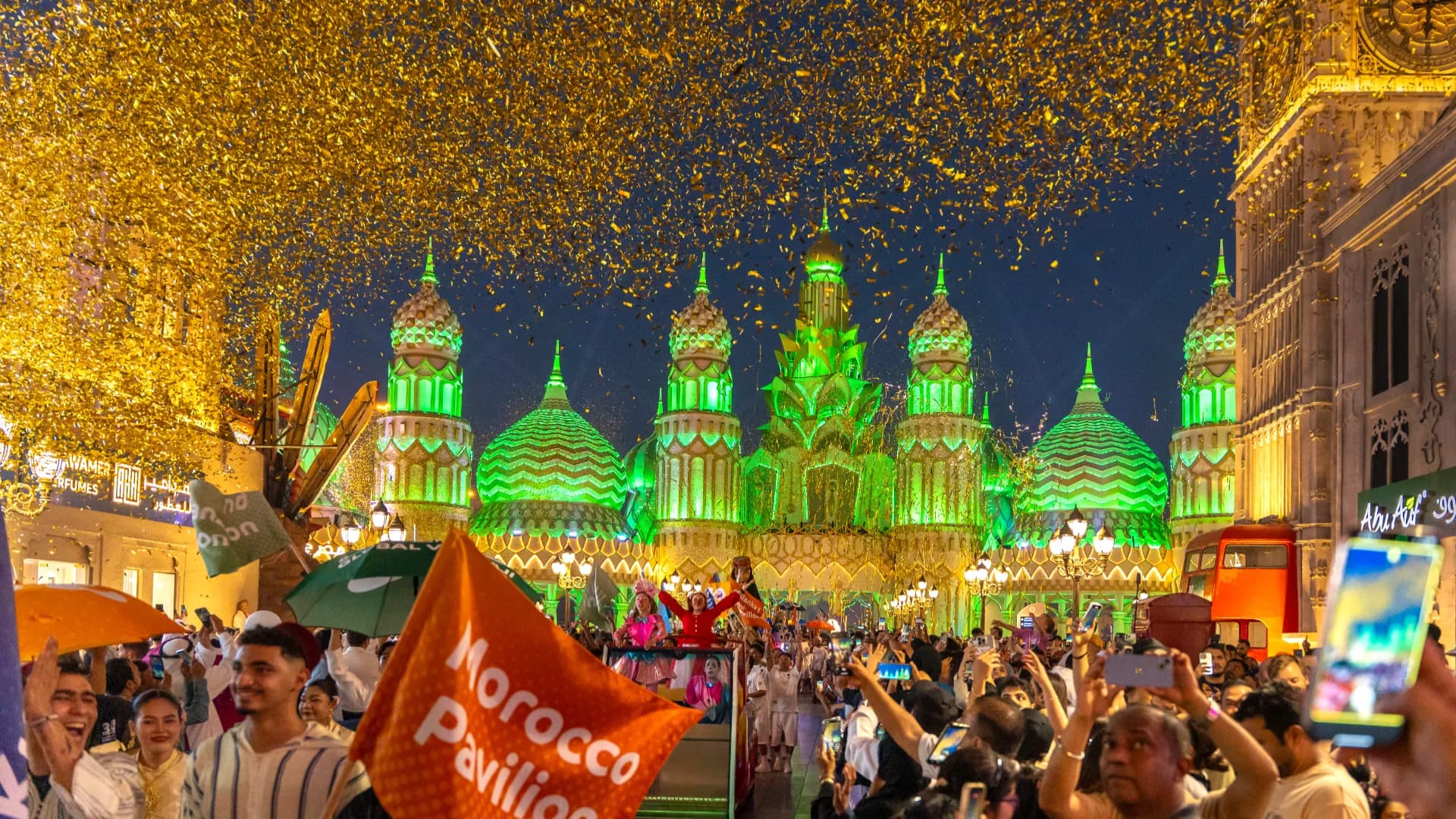 Visitors walking between the lit pavilions at Global Village in the evening